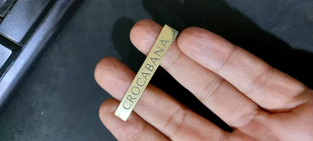 Thin brass bar label engraved Crocabana held between fingers