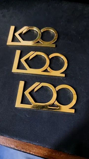 Three cut-out brass logo pieces in the KOO design